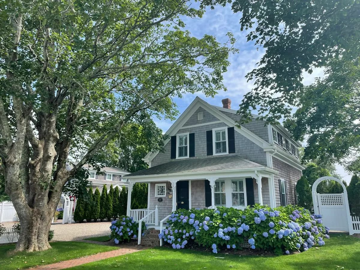 Deep covered porch on a blue house surrounded by trees
